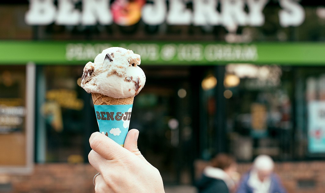close-up of woman holding up ice cream cone in front of Ben & Jerry's store